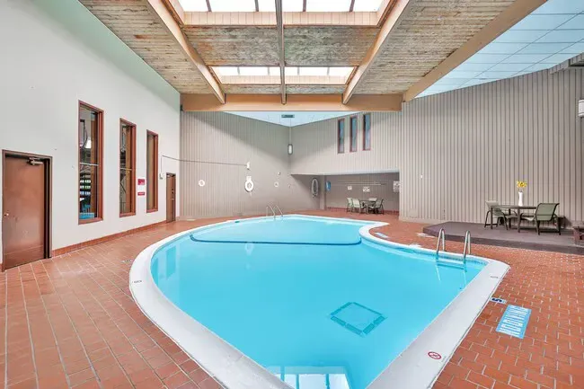 Indoor pool with blue water, brick floor, wooden ceiling, and windows.