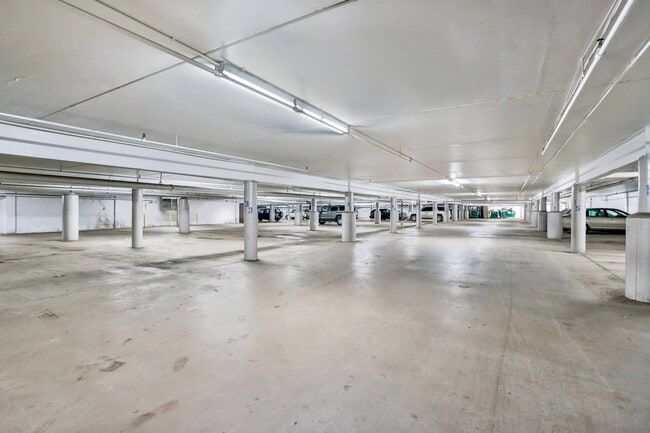 Empty parking garage with concrete floor and support pillars. Fluorescent lights illuminate the space.
