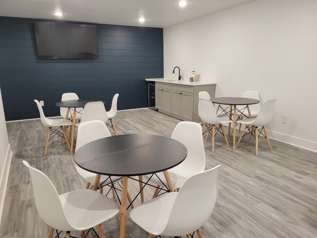 Modern room with round tables, white chairs, a blue accent wall, and a small bar area.