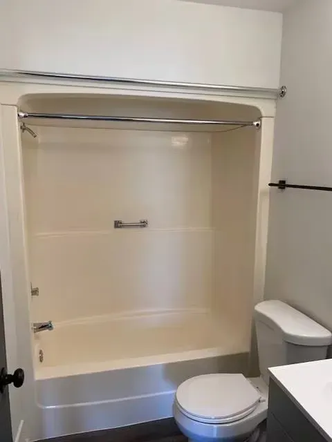 Bathroom with cream-colored tub/shower, toilet, and a black towel bar.