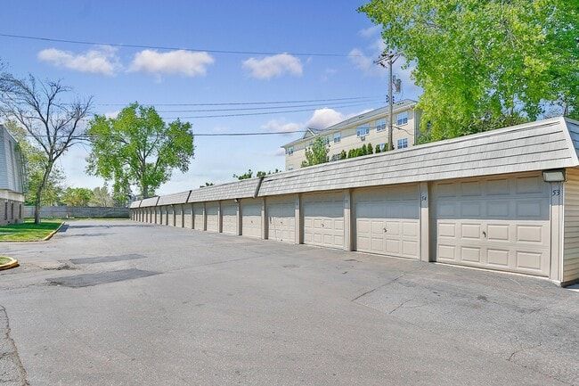 Row of beige garages with gray roofs and a paved driveway, under a blue sky.