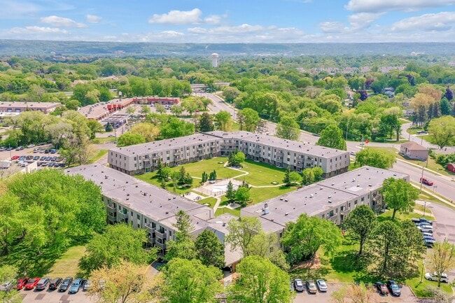 Aerial view of apartment complex with green courtyard surrounded by trees, blue sky overhead.