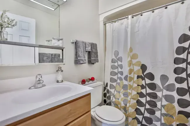 Bathroom with white sink, light brown cabinet, gray towels, and a shower curtain with yellow and gray leaf design.