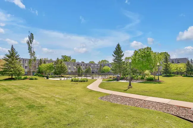 Green lawn with a winding stone path leading toward an apartment building on a sunny day.