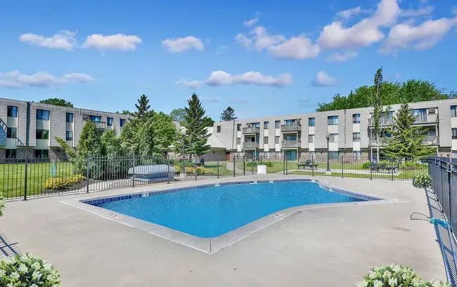 A swimming pool in front of a multi-story apartment building under a blue sky.