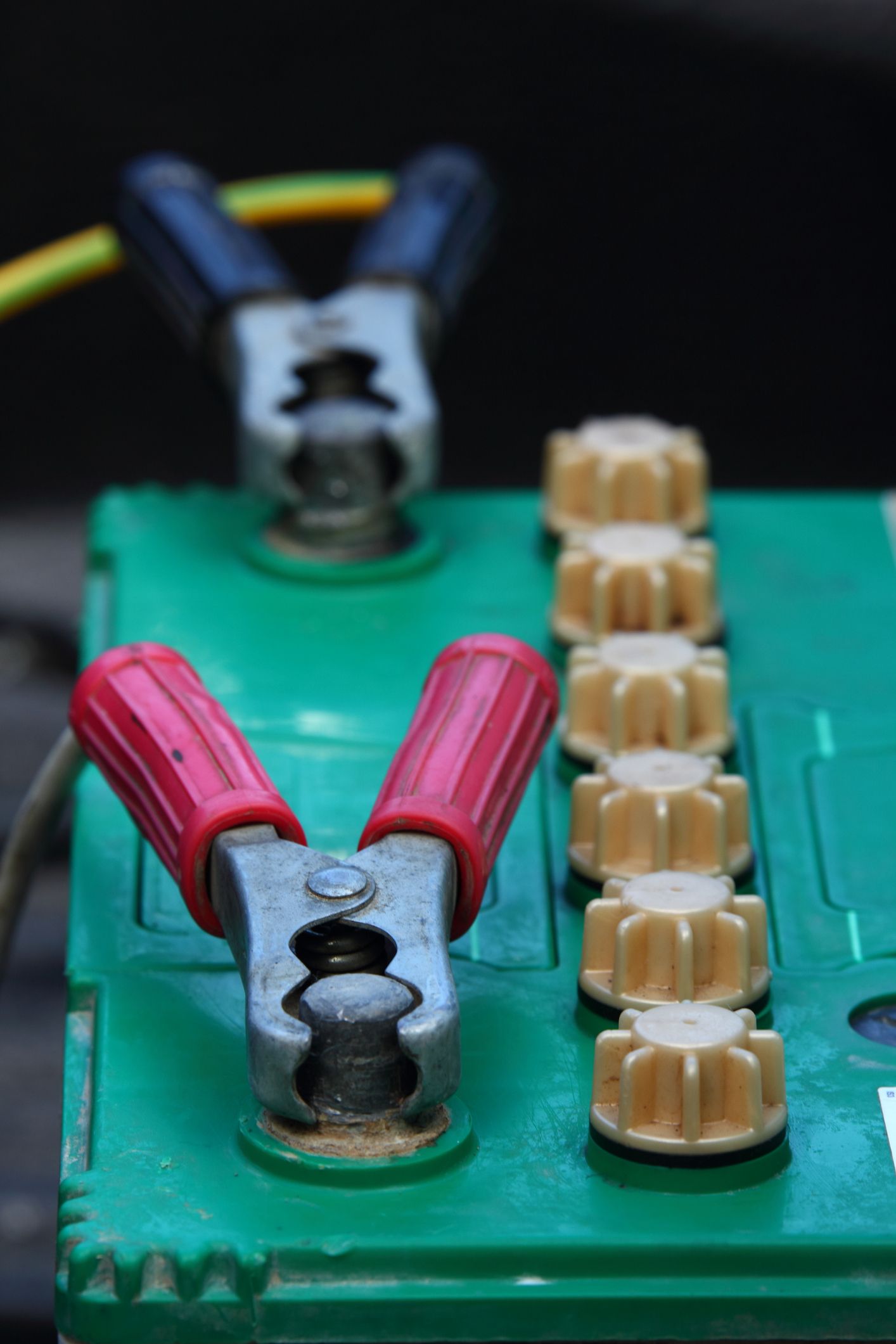A green battery with a pair of clamps attached to it