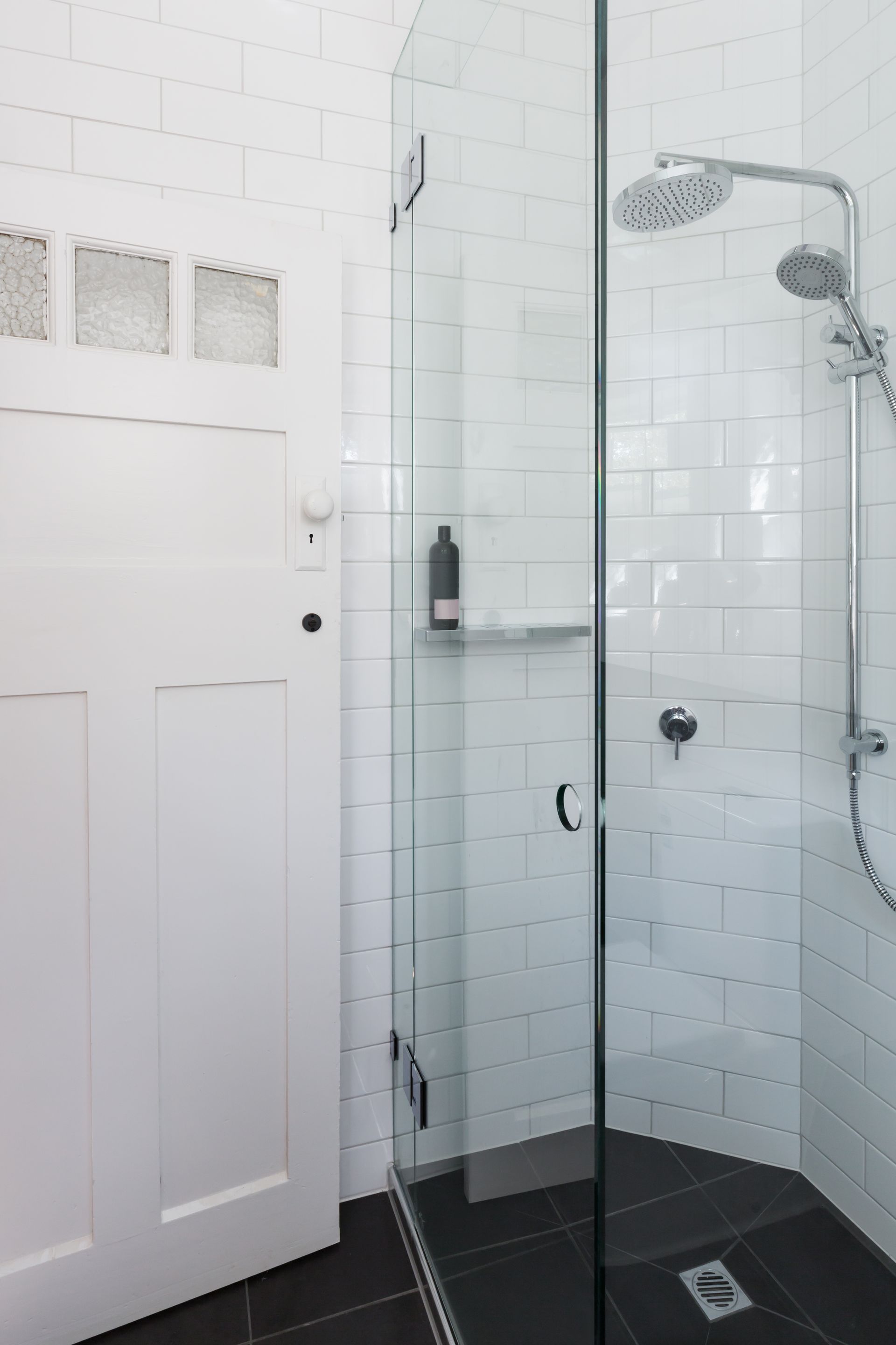 A walk-in shower with white subway tiles and a glass door next to a white wooden door with frosted glass panels.