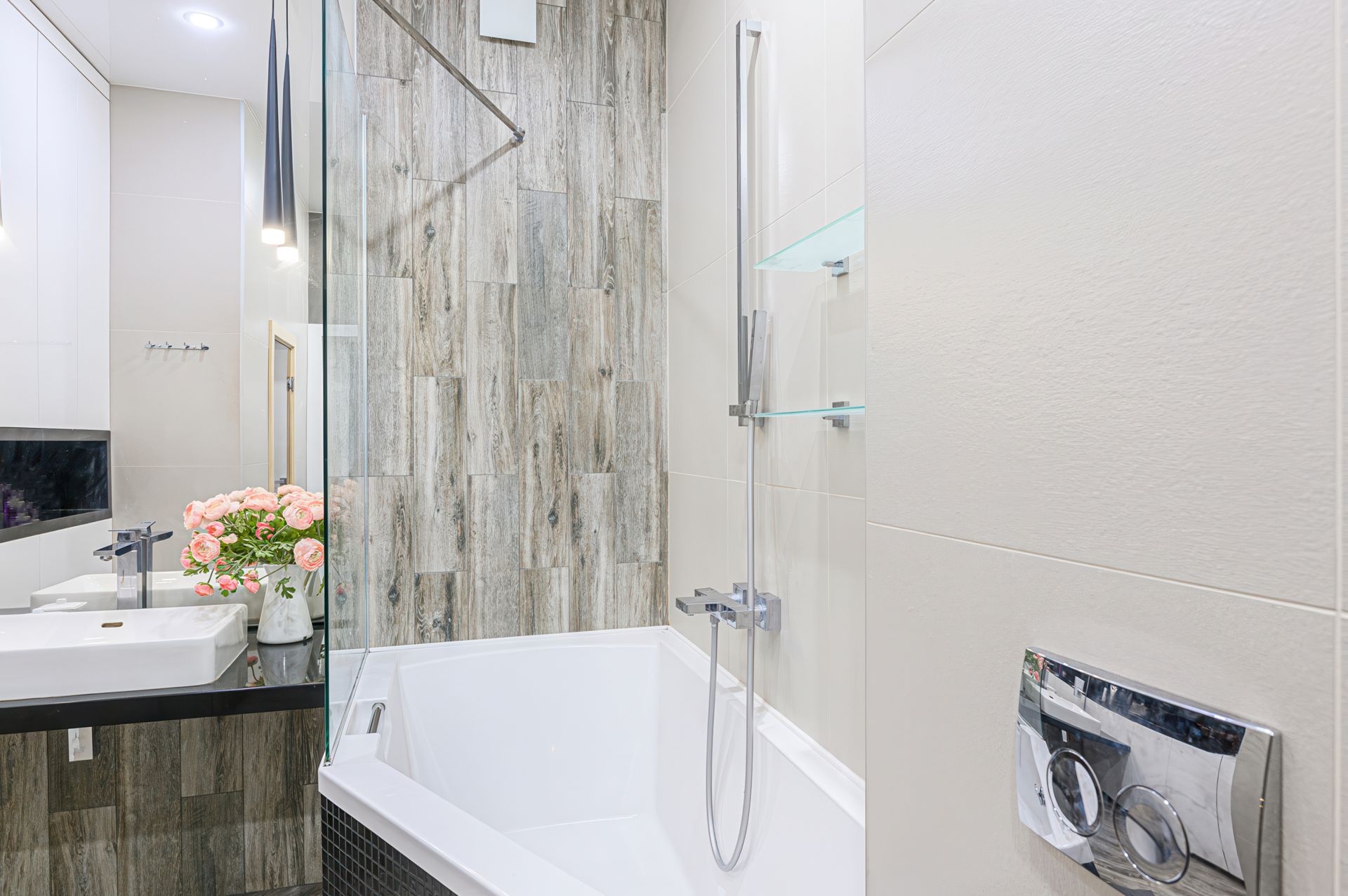 A modern bathroom featuring a white bathtub, a sink with a vase of pink flowers, and textured, wood-look tiled walls.