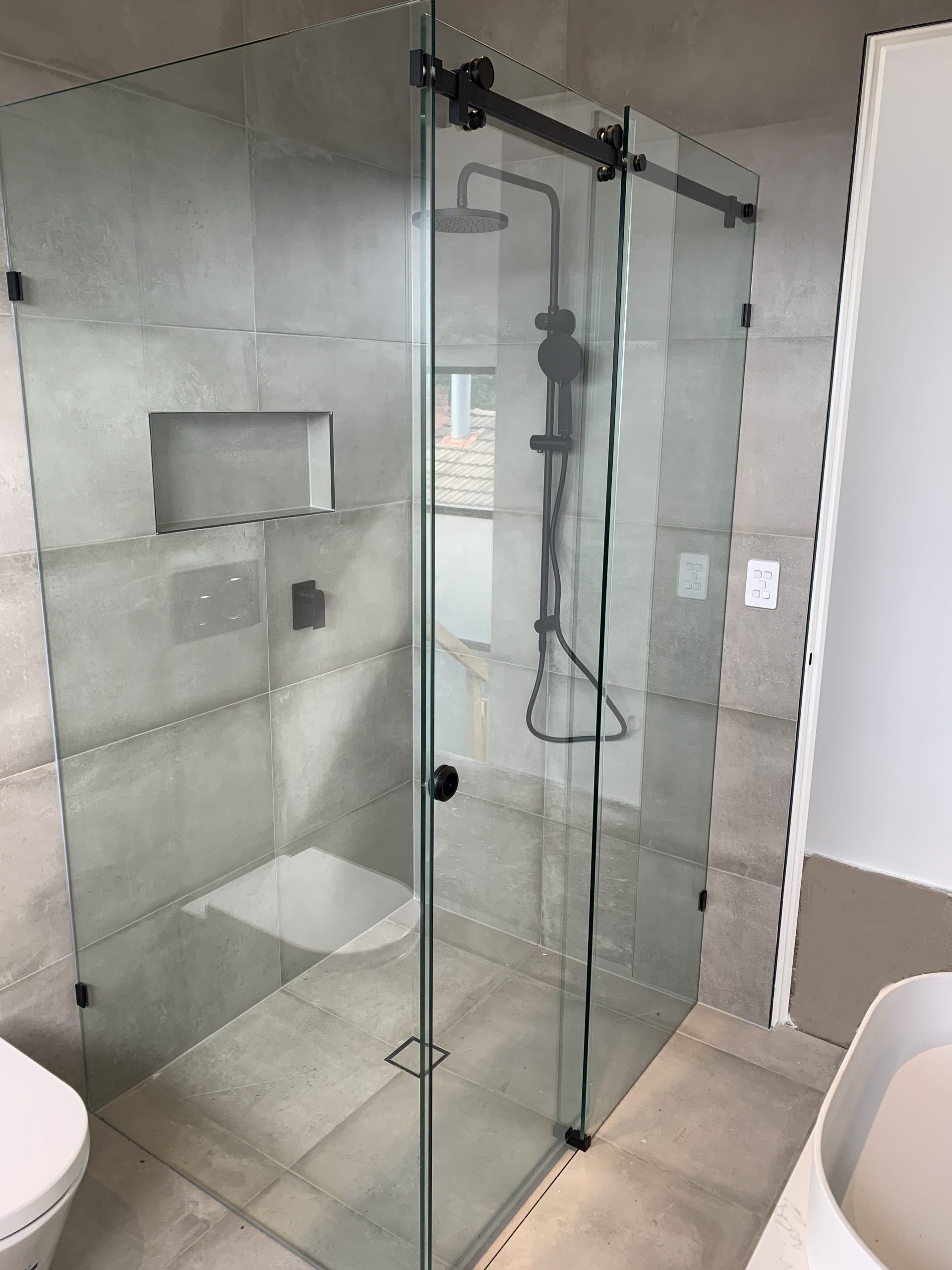 A modern white bathroom with a freestanding tub, gold fixtures, marble tile floors, and a glass-enclosed shower.