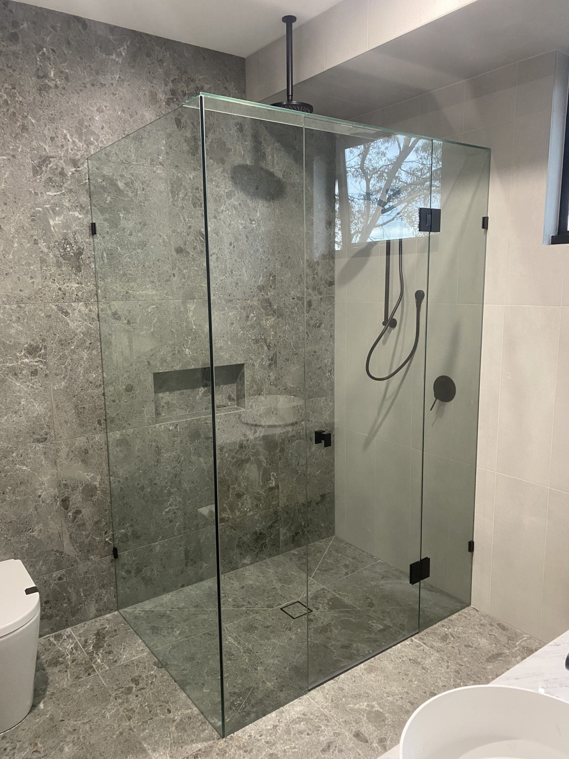 A modern bathroom with a glass-enclosed shower, a double vanity with wood-grain cabinets, and gold fixtures.