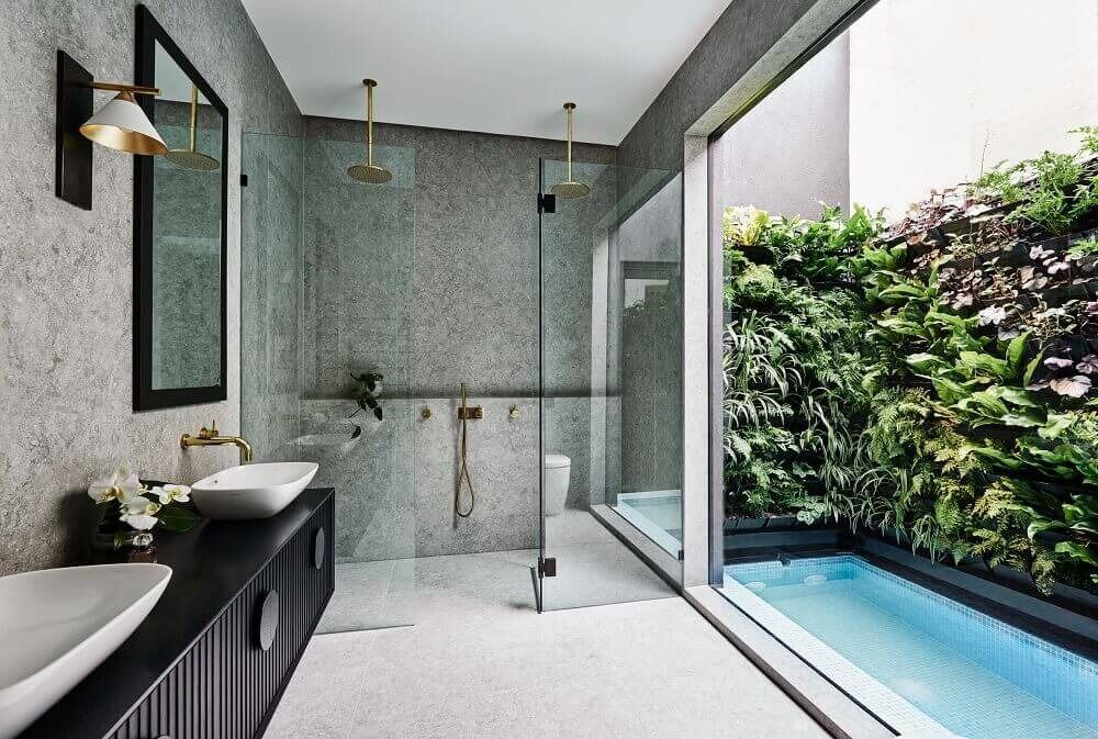 A modern, bright bathroom with a white bathtub against a grey stone wall, a sink area, and a large frosted glass partition.
