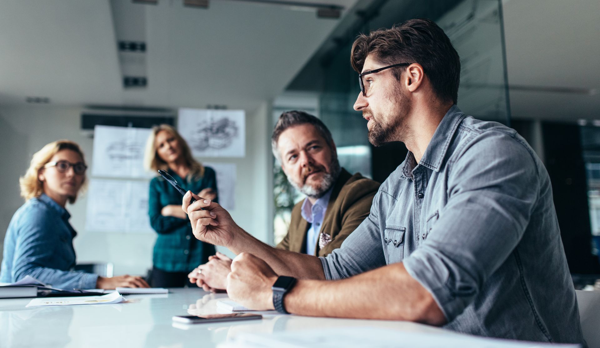 a group of business people are sitting around a table having a meeting .