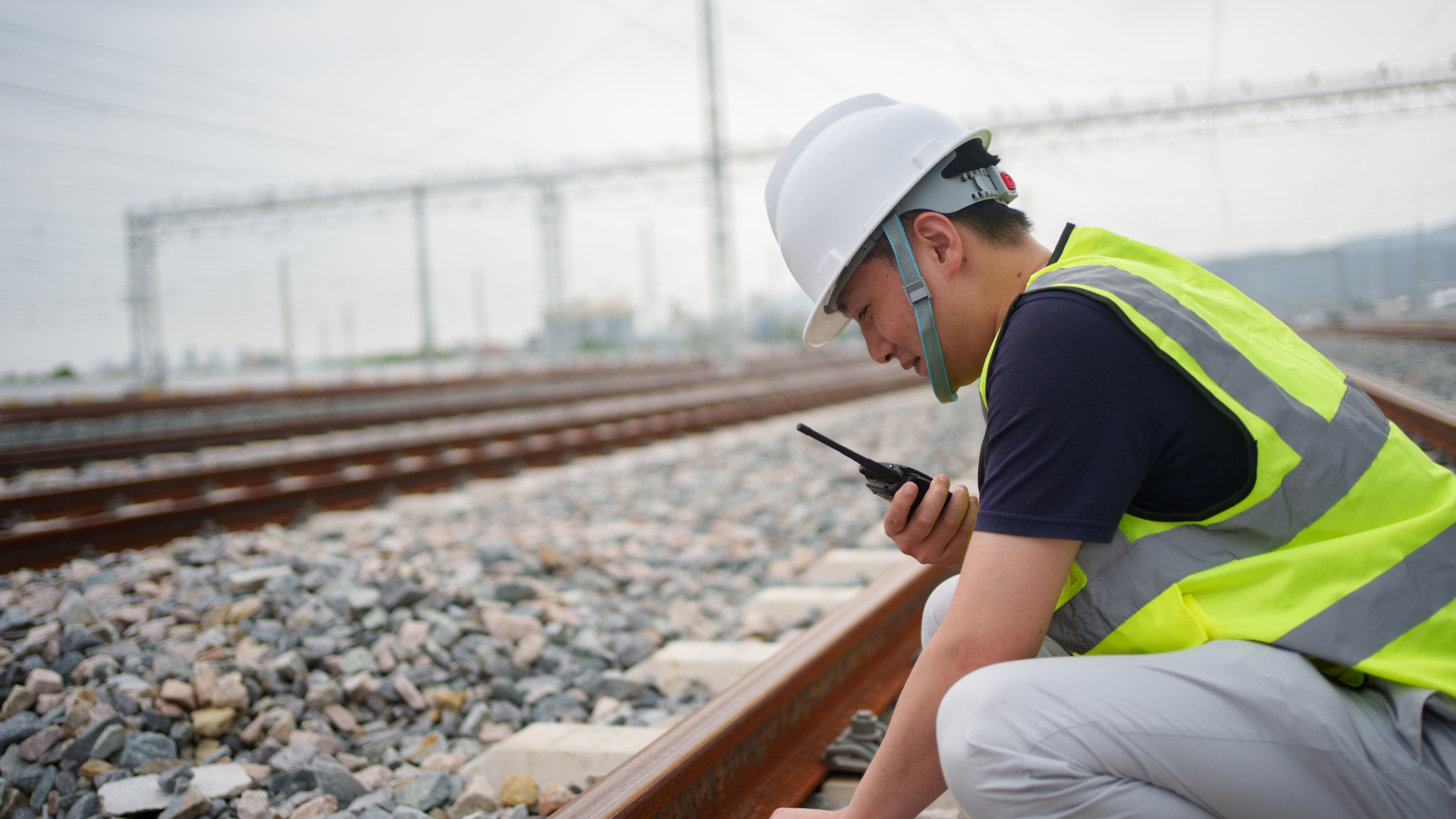A man is kneeling on train tracks while talking on a walkie talkie.