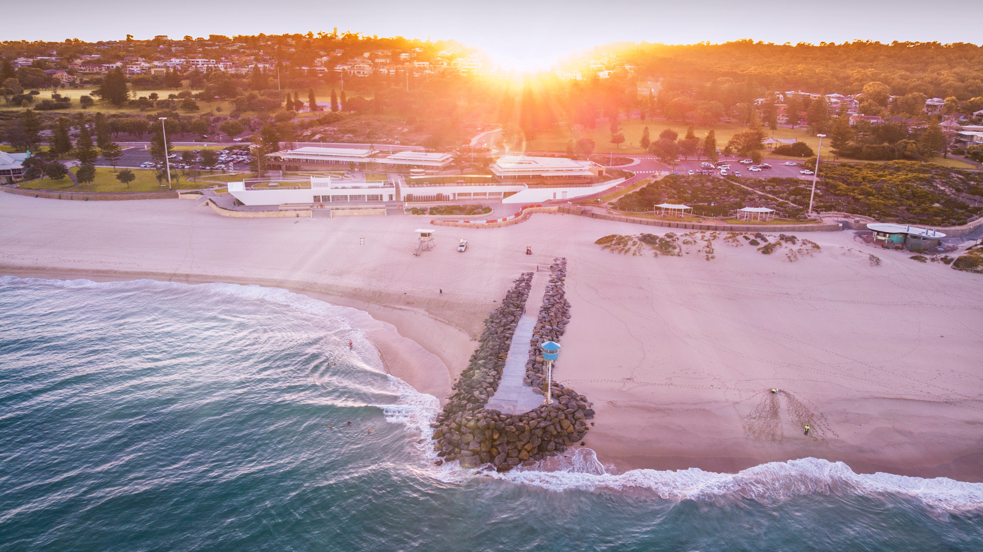 An aerial view of a beach at sunset with a pier in the foreground.