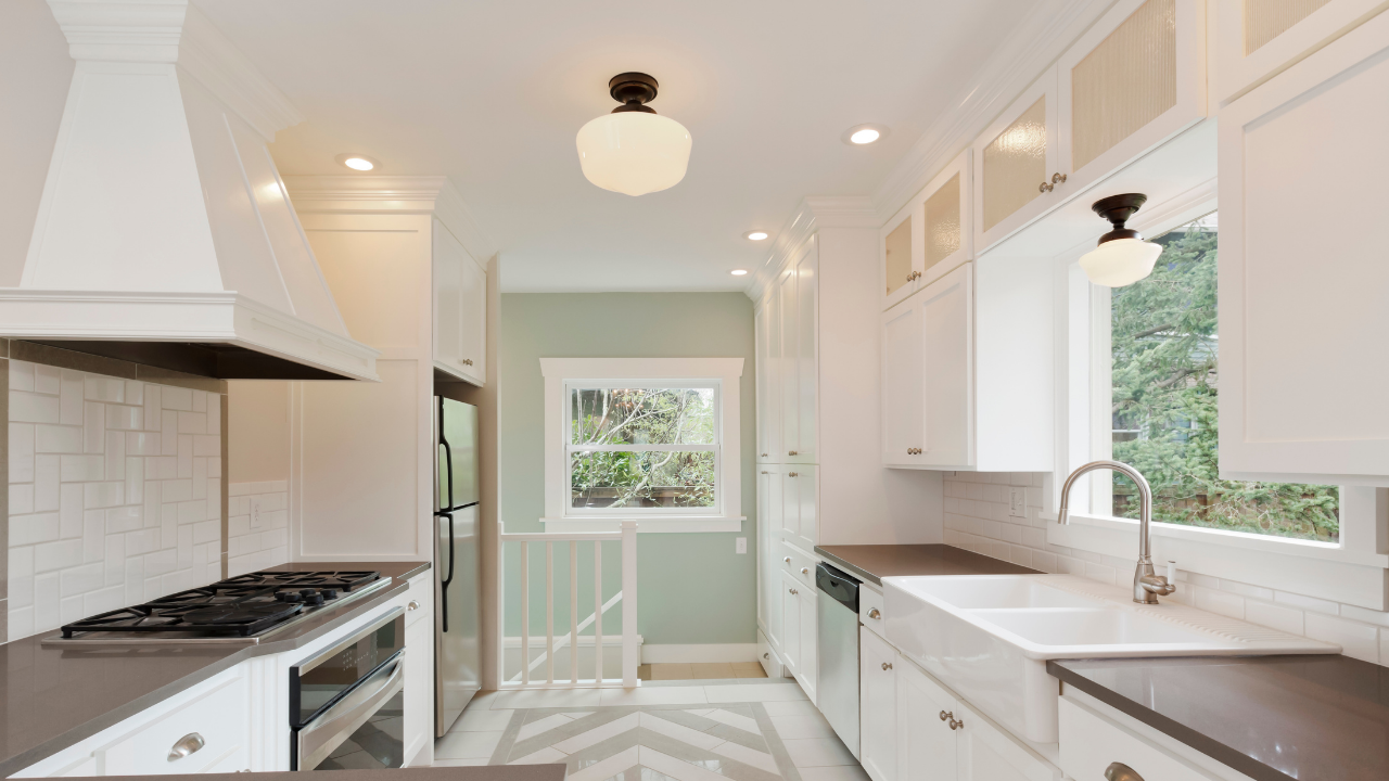 Bright white galley kitchen with black countertops, stainless stove, and a window over the sink.
