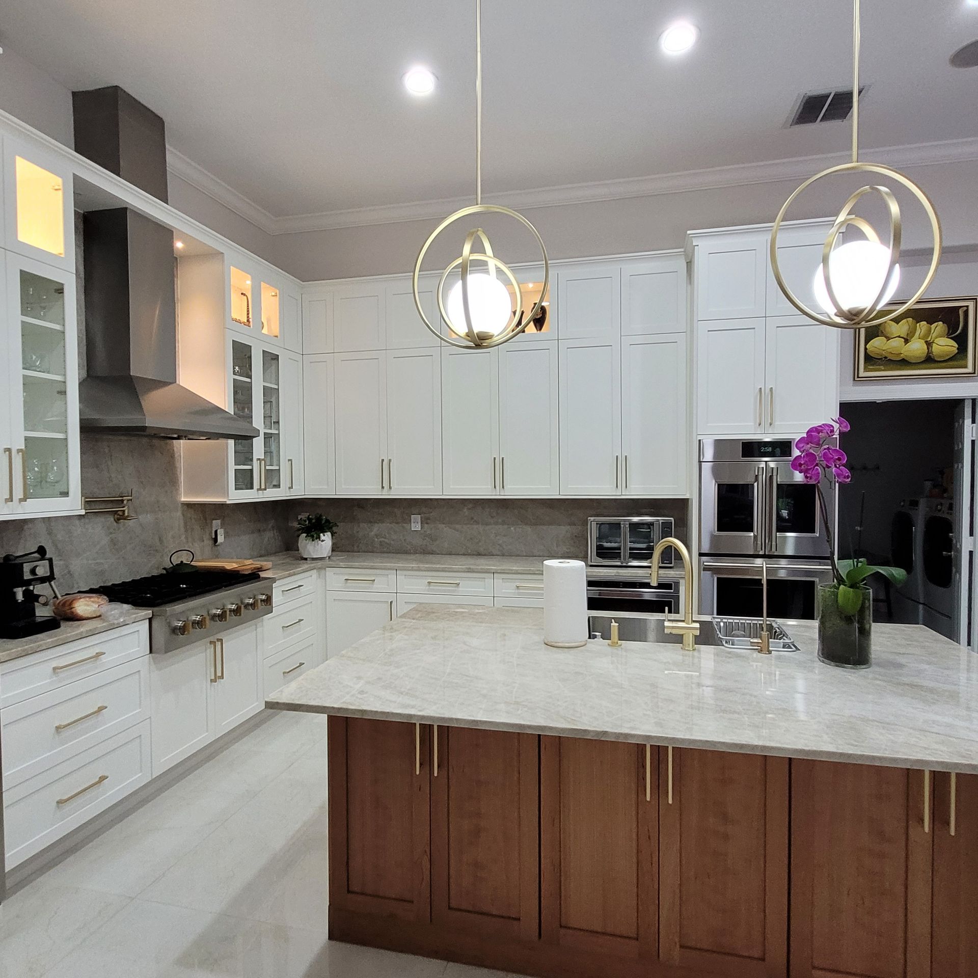 Bright modern white kitchen with marble island, wood cabinets, pendant lights, and built-in appliances