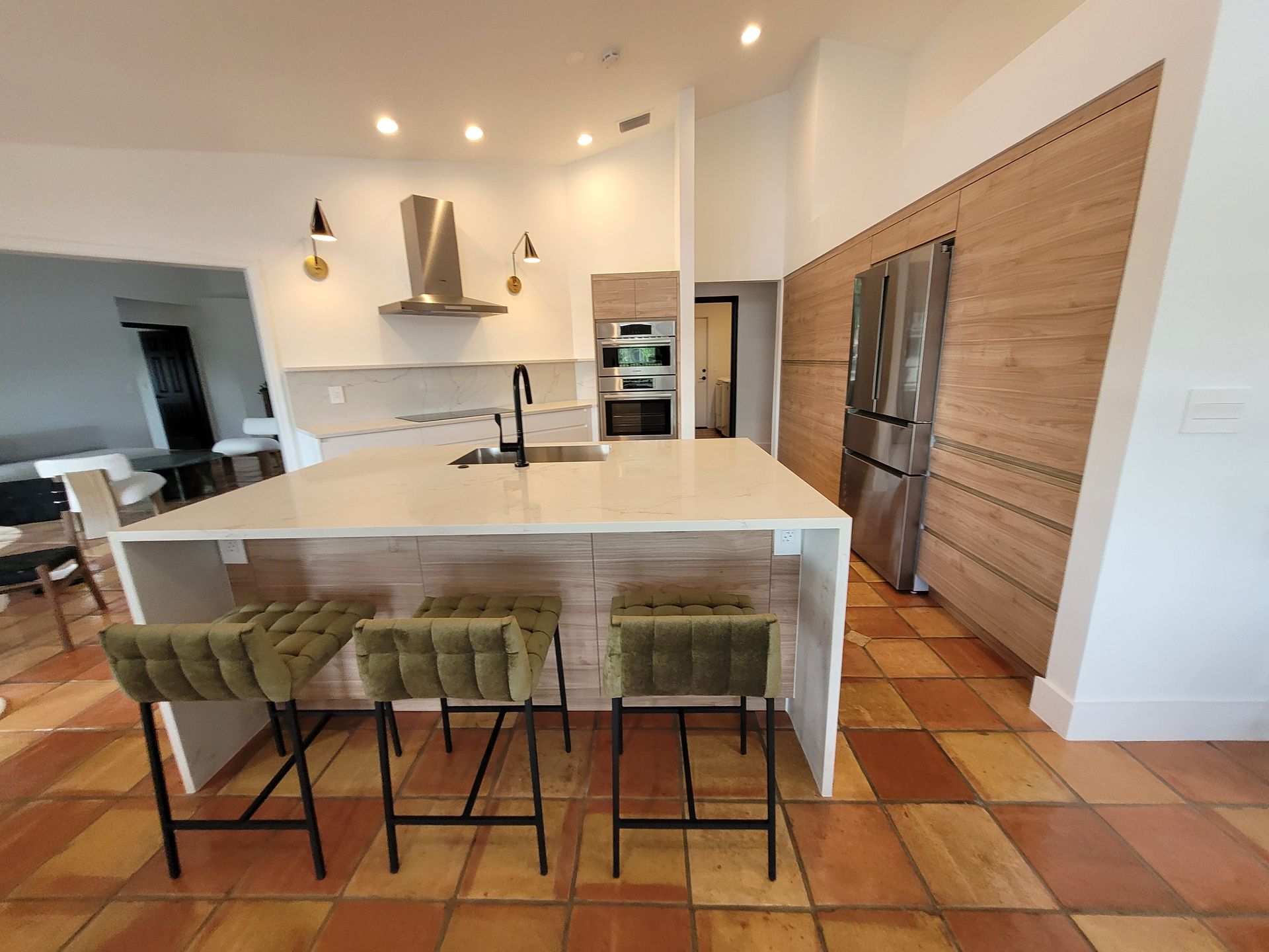 Modern kitchen with white island, green stools, and terracotta tile floor