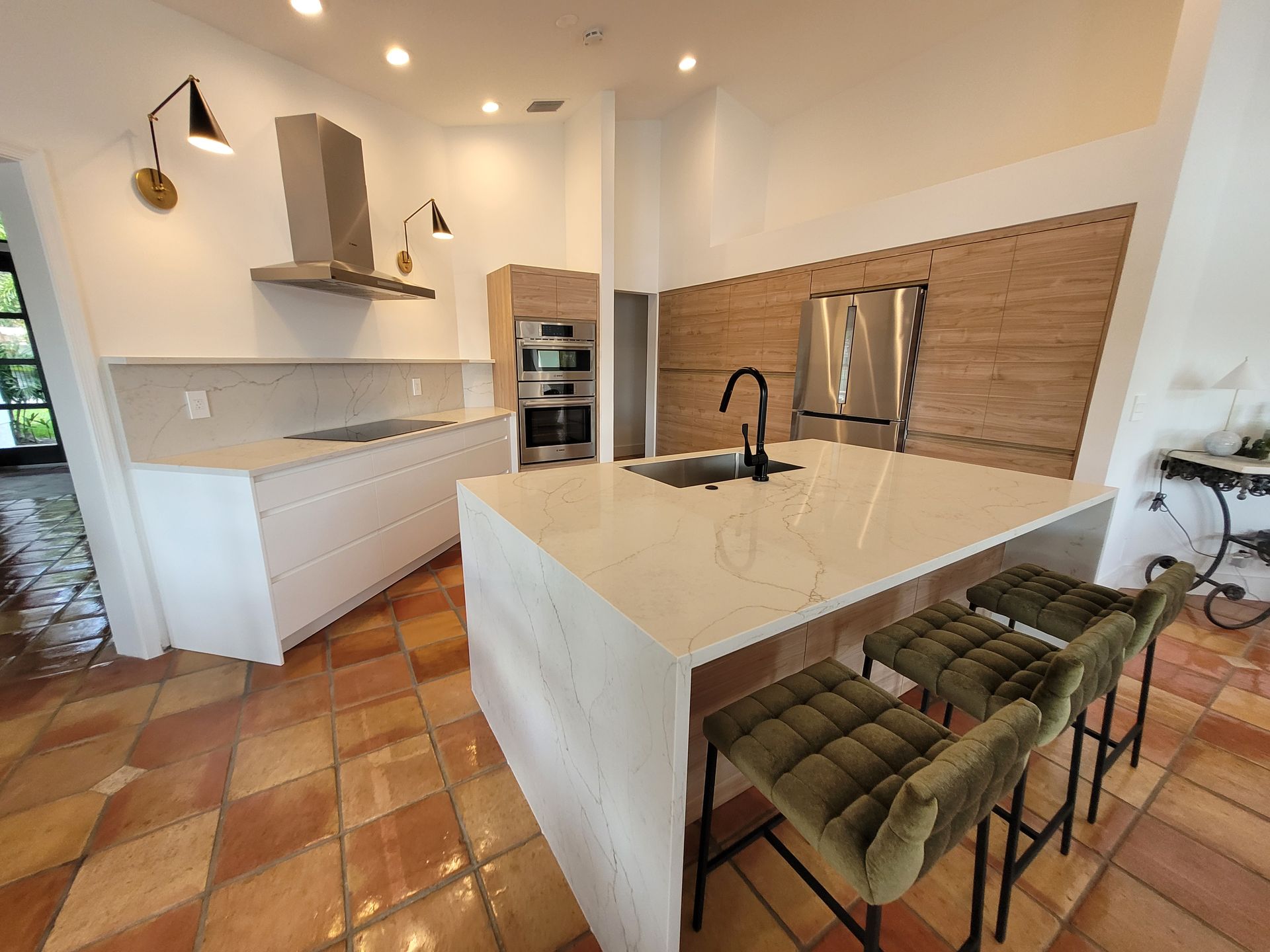 Modern kitchen with white cabinets, marble island, green bar stools, and wood tile flooring.
