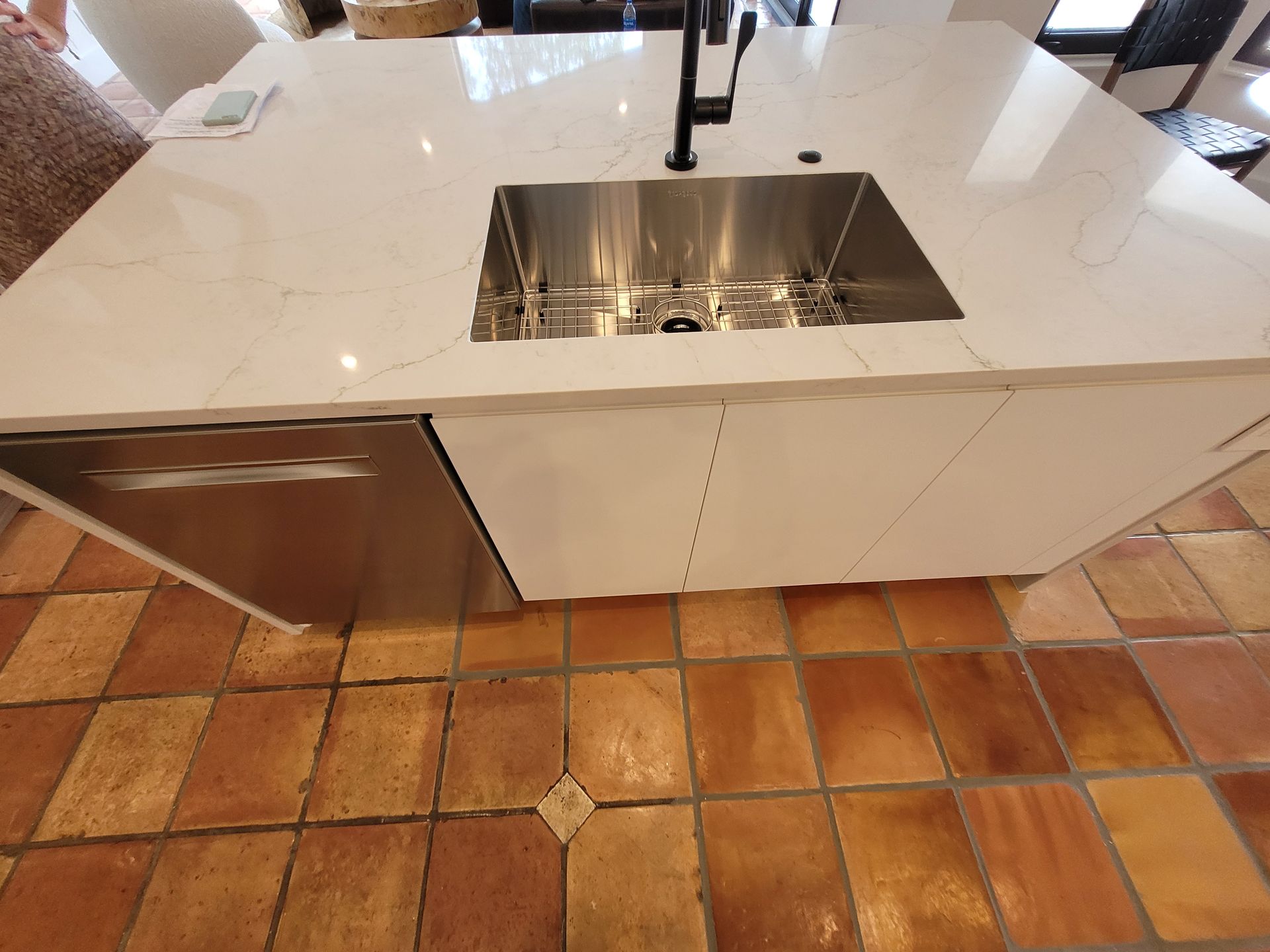 Modern kitchen island with stainless sink and faucet, white marble countertop, and terracotta tile floor