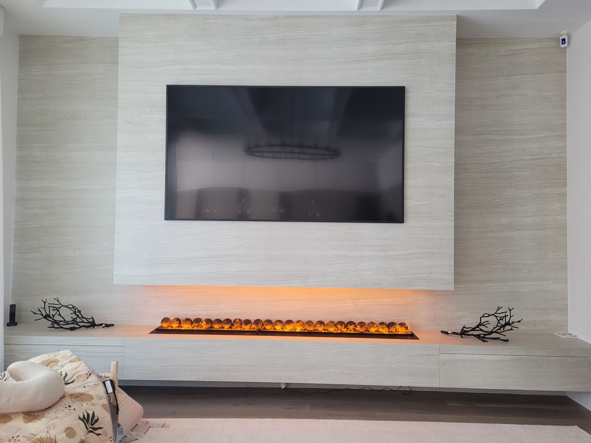 Modern minimalist living room with a wall-mounted TV above a long linear fireplace and light wood accents