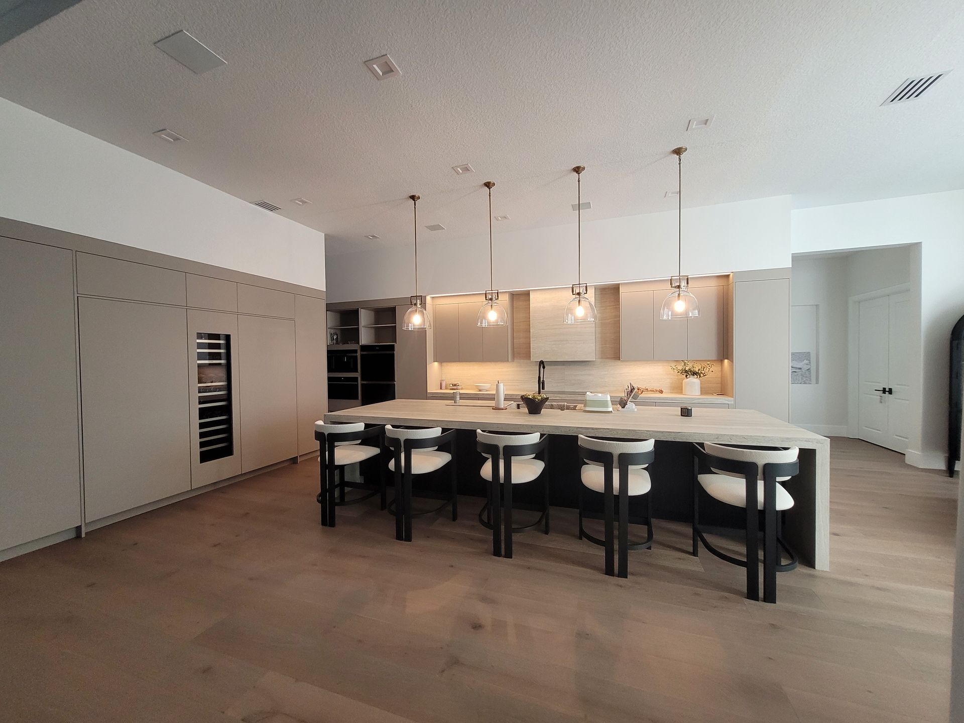 Modern kitchen with large island, black stools, pendant lights, and light wood cabinetry