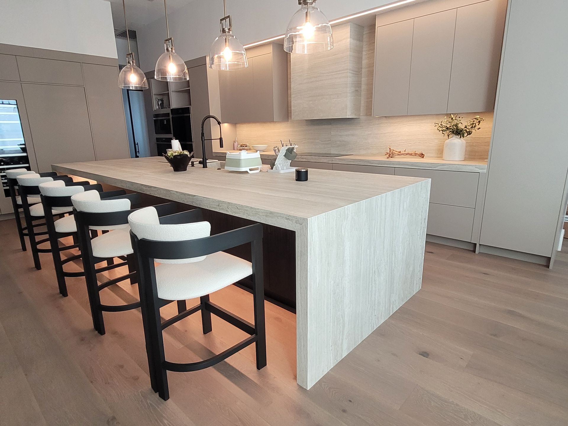 Modern kitchen with large island, bar stools, pendant lights, and light wood cabinetry