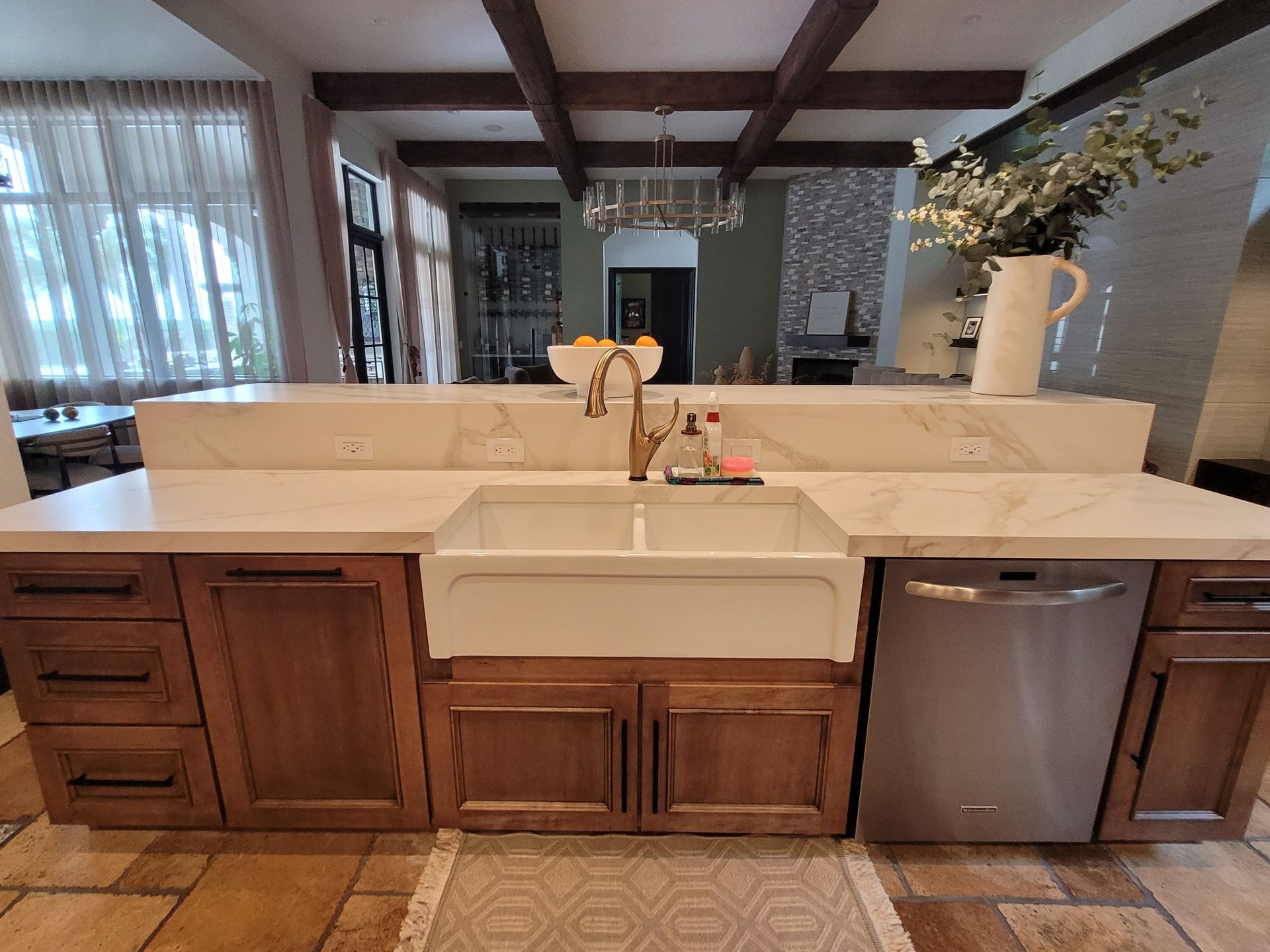 Kitchen island with white countertop, apron sink, wood cabinets, and stainless dishwasher in a bright home interior