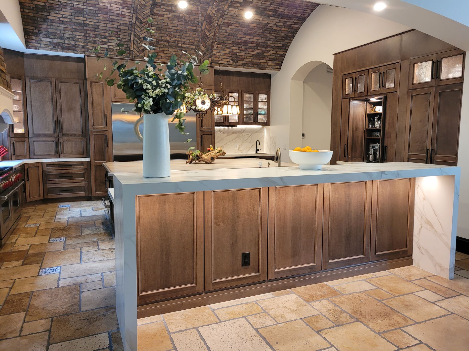 Rustic kitchen with wood cabinets, a marble island, tiled floor, and a vase of flowers on the counter