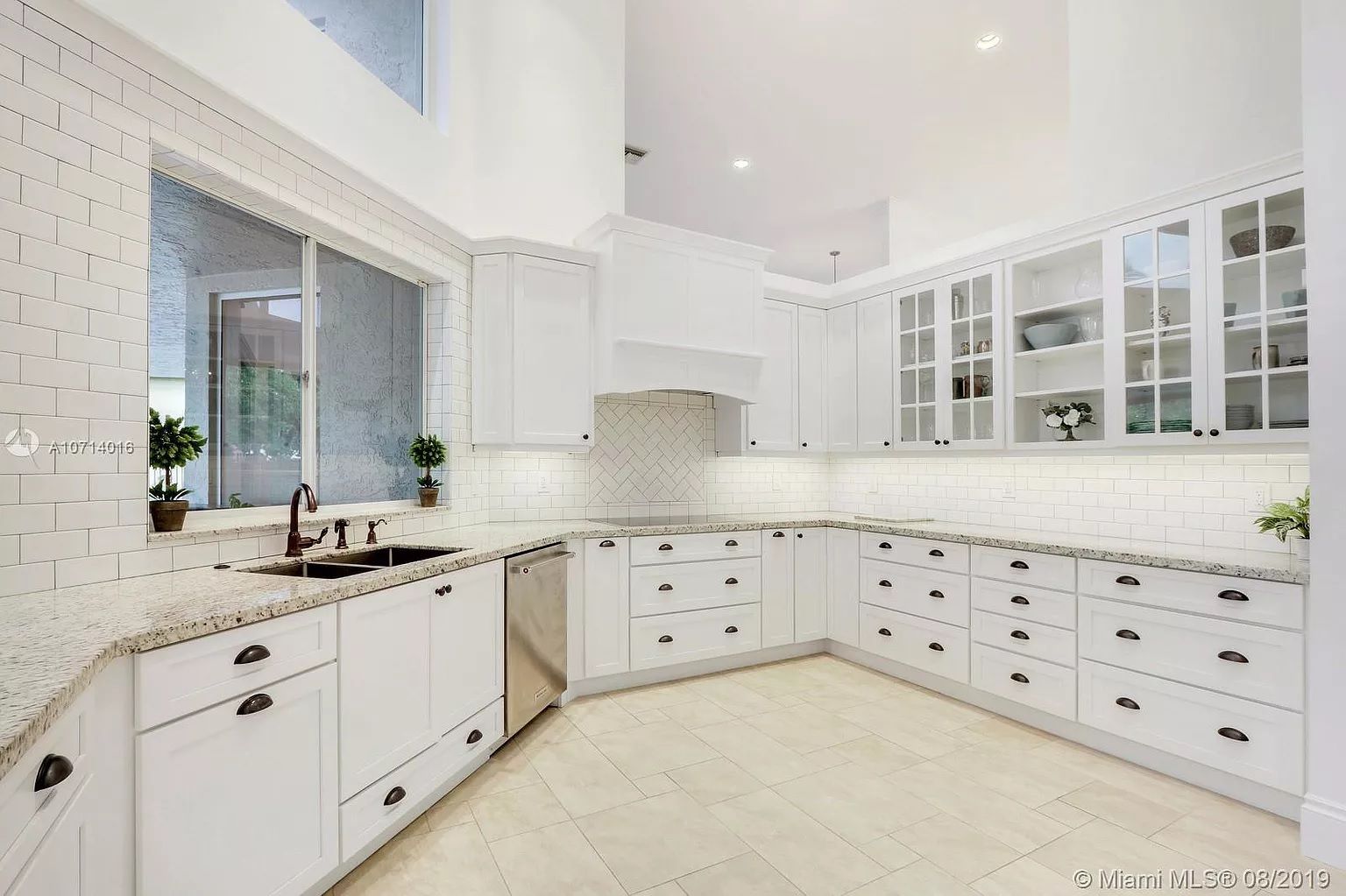 Bright white modern kitchen with shaker cabinets, marble countertops, and large window over the sink