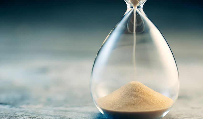 An hourglass with sand settled in the bottom bulb on a soft gray surface.
