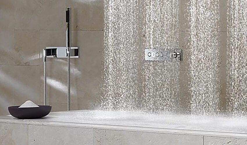Minimalist bathroom shower with rainfall water falling beside a wall-mounted faucet.