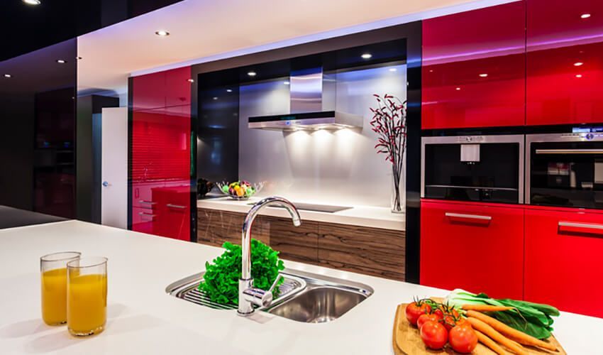 Modern red-and-black kitchen with white island, sink, fruit, and glasses of orange juice