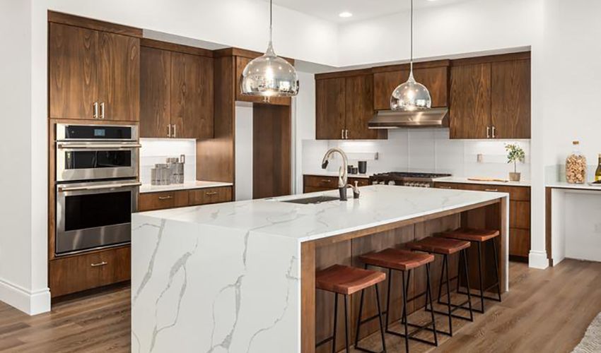 Modern kitchen with white marble island, wood cabinets, stainless appliances, and barstools under pendant lights