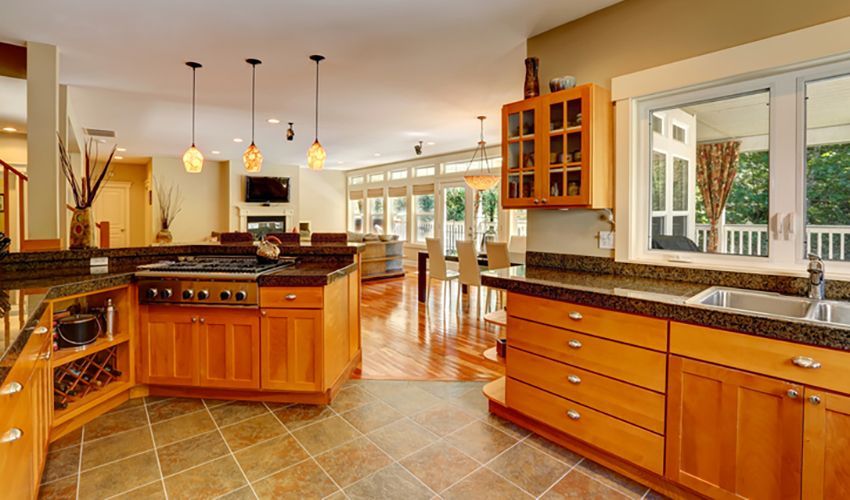 Spacious modern kitchen with wooden cabinets, granite counters, tiled floor, and large windows overlooking greenery