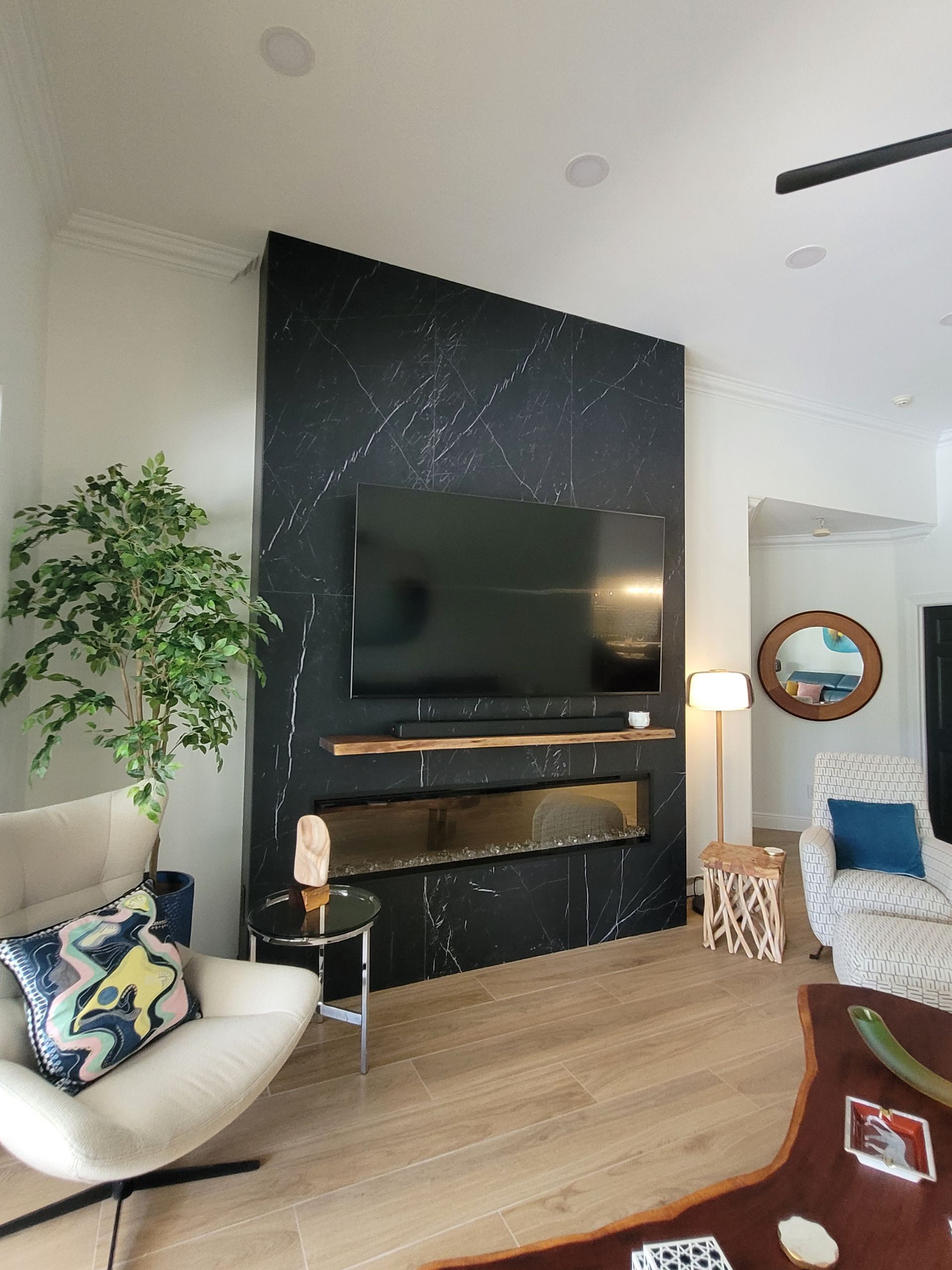 Modern living room with black fireplace wall, TV, white chair, and wooden floors