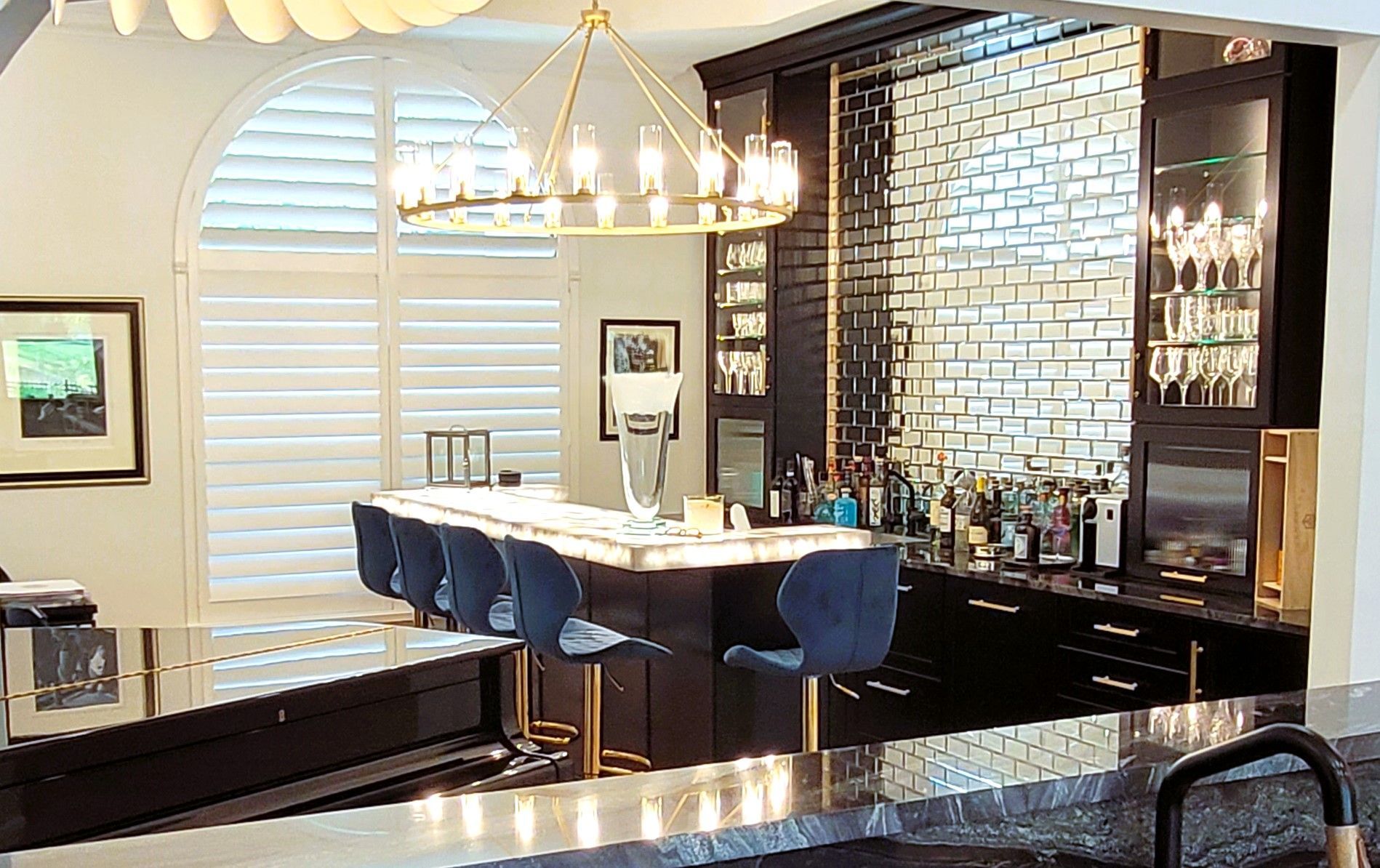Modern kitchen with granite island, blue bar stools, chandelier, and brick accent wall