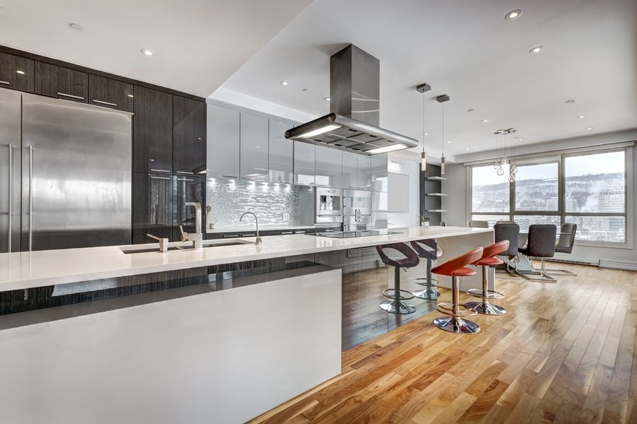 Modern open kitchen and dining area with stainless steel appliances, bar stools, and hardwood floors