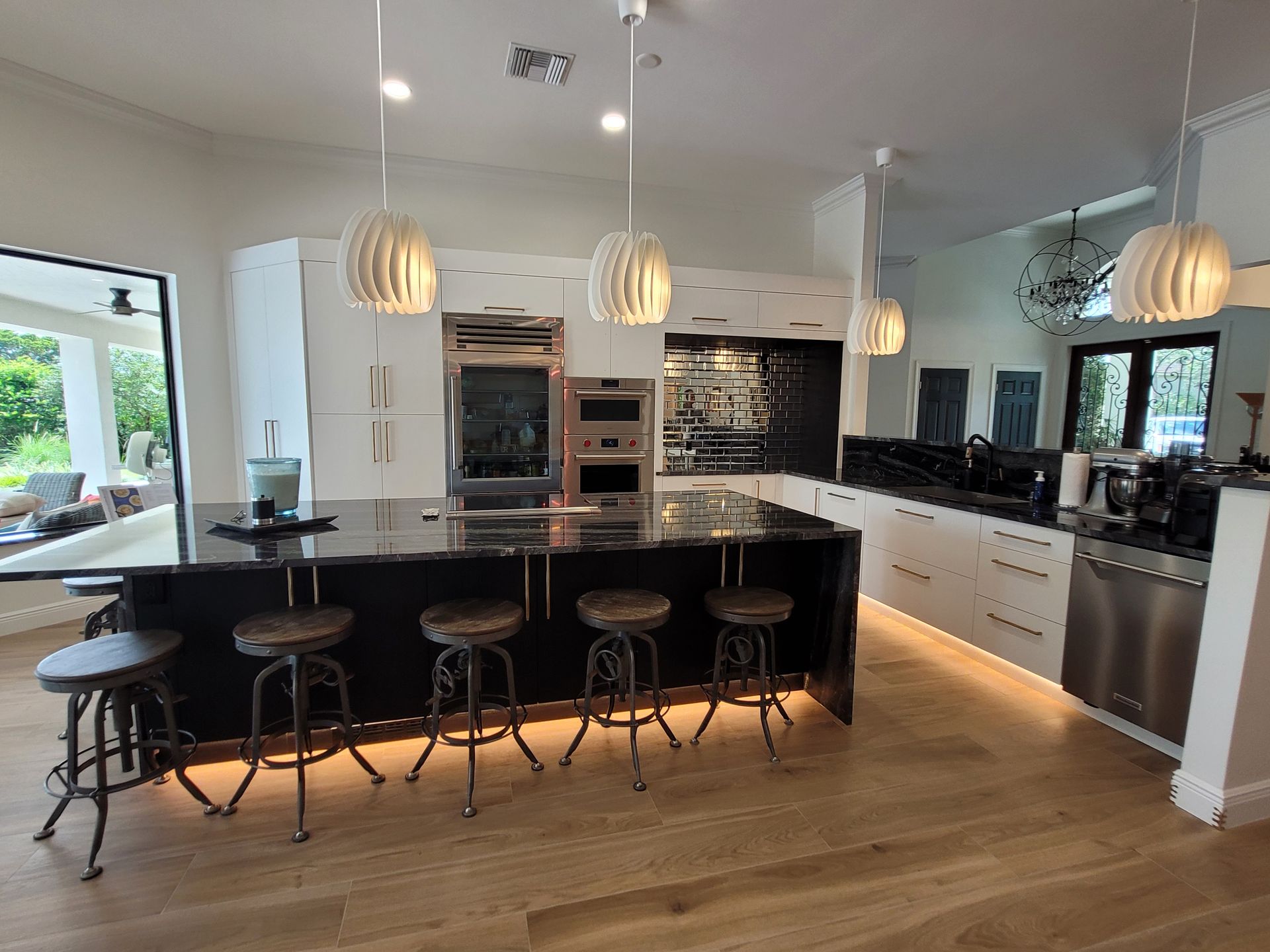 Bright modern kitchen with black island, pendant lights, bar stools, and stainless steel appliances.