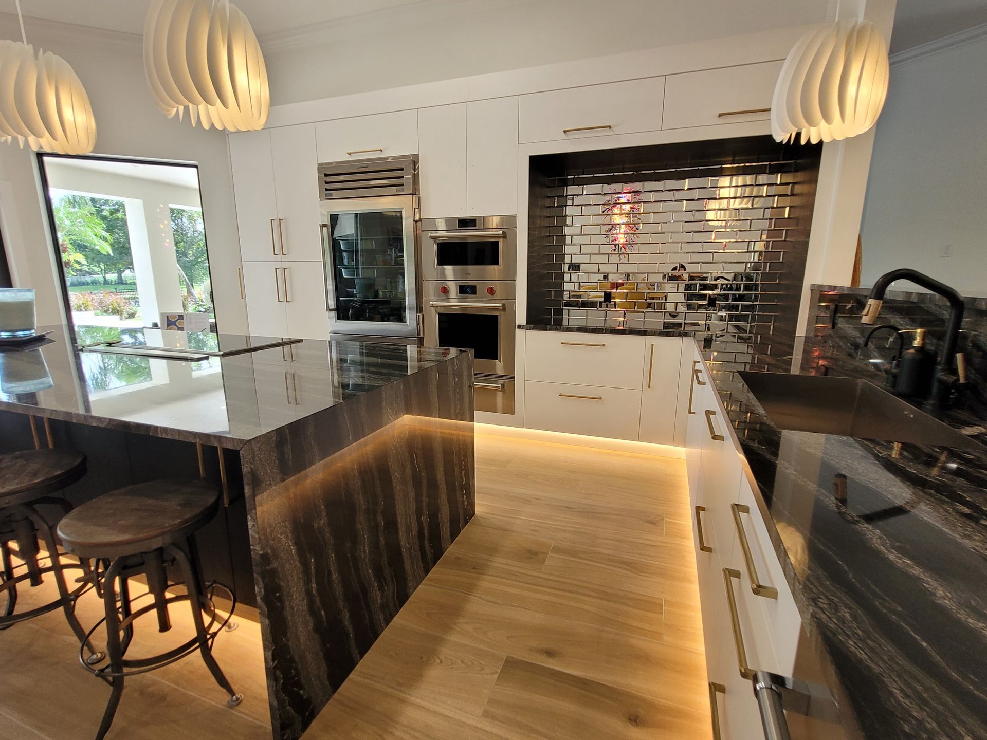 Modern kitchen with black countertops, wood island, white cabinets, pendant lights, and brick backsplash.