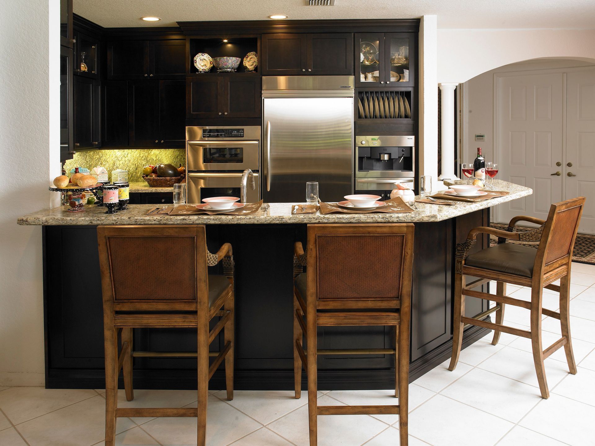 Modern kitchen with dark cabinets, stainless steel appliances, and a breakfast bar with three stools