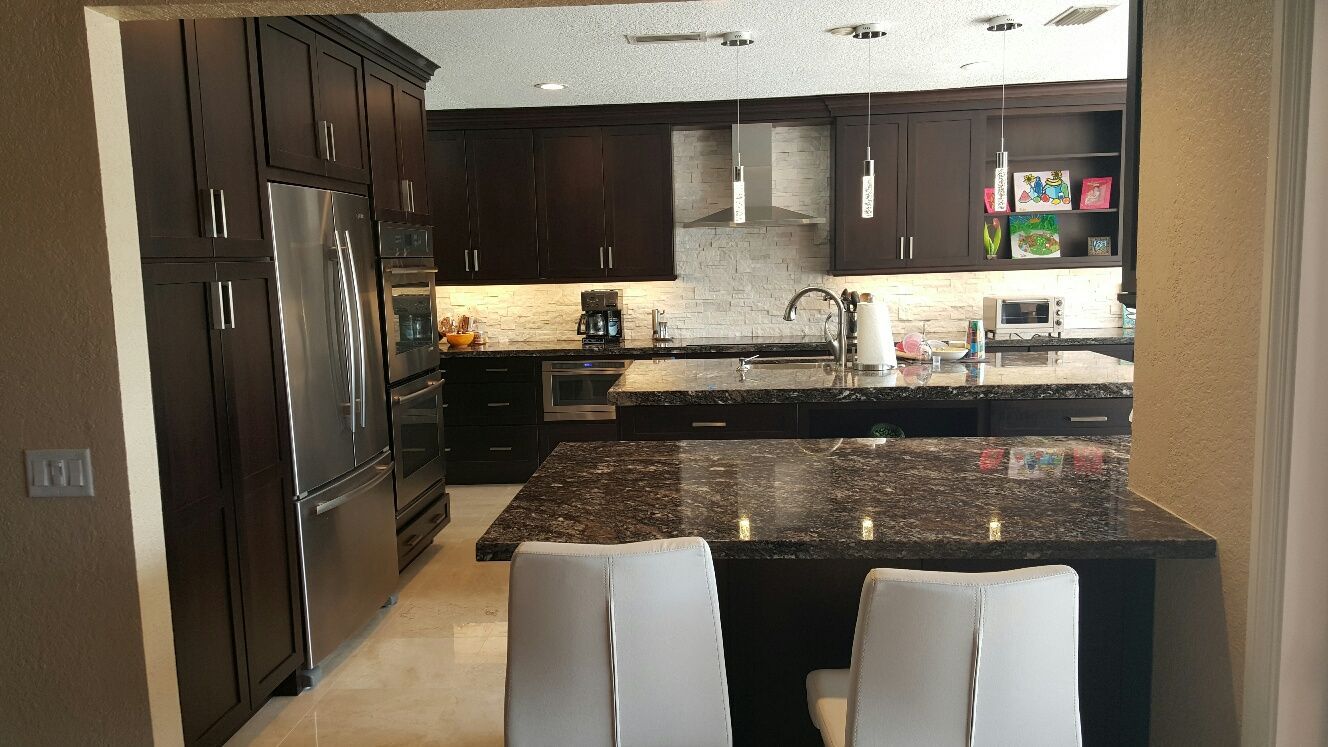 Modern kitchen with dark cabinets, granite island, and two white bar stools.