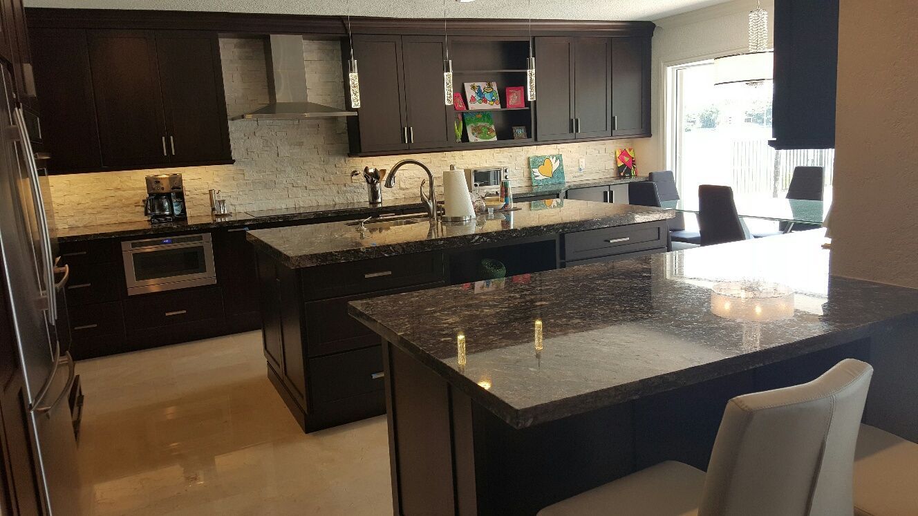 Modern kitchen with dark cabinets, granite island, and stainless appliances, seen from the dining area