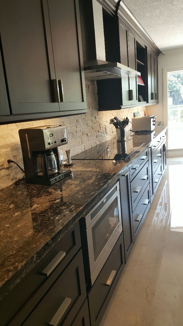 Modern kitchen with dark cabinets, granite countertops, coffee maker, and stainless steel appliances along a bright hallway