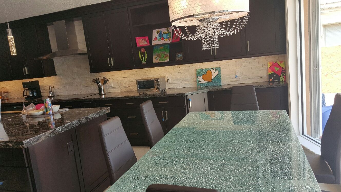 Modern kitchen and dining area with dark cabinets, granite table, and chandelier lighting