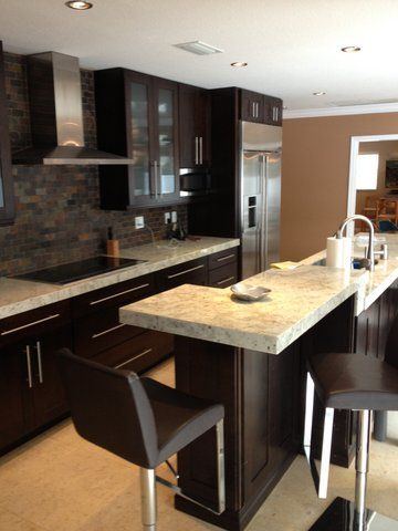 Modern kitchen with dark cabinets, stainless appliances, and a granite island with bar stools