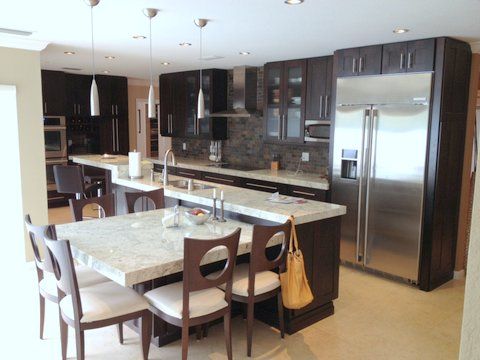 Modern kitchen with dark cabinets, stainless steel appliances, and a marble island with dining chairs