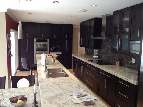 Modern kitchen with dark cabinets, granite counters, and a central island with a sink and faucet.