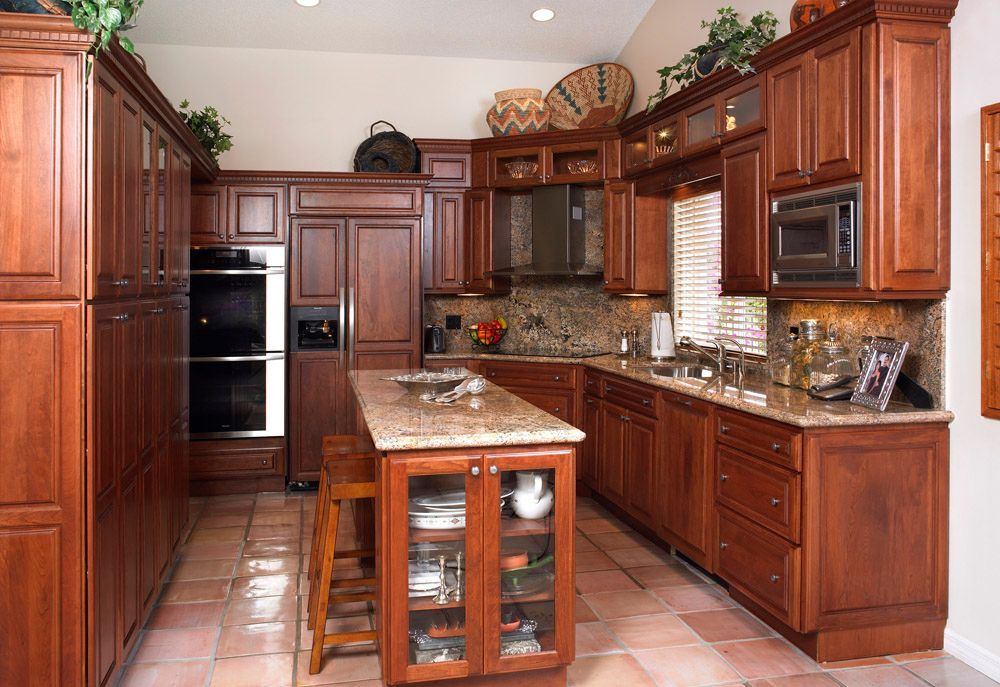 Warm wood kitchen with central island, tiled floor, built-in ovens, and granite countertops
