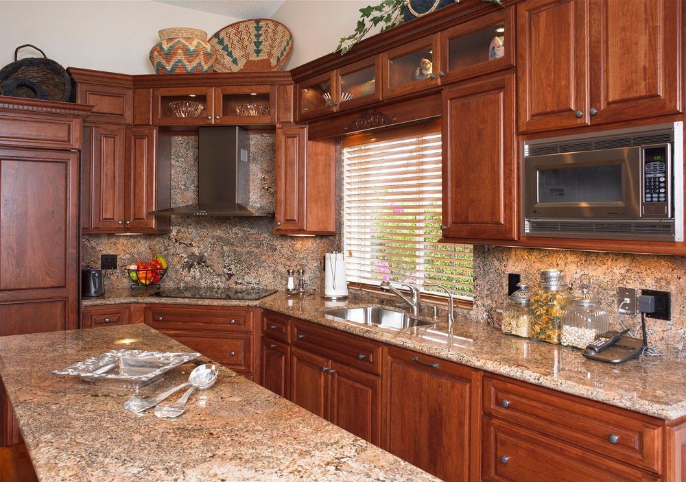 Warm kitchen with dark wood cabinets, granite counters, mosaic backsplash, and a large window over the sink