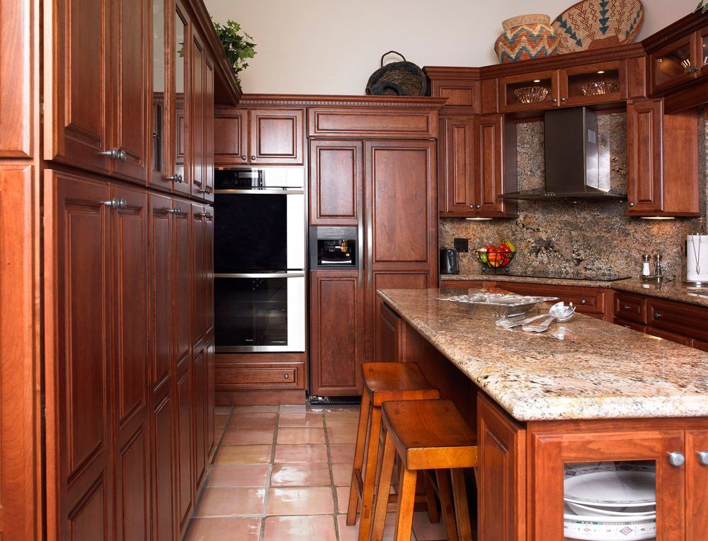 Warm-toned kitchen with cherry wood cabinets, granite counters, and a tiled floor, viewed from the aisle.